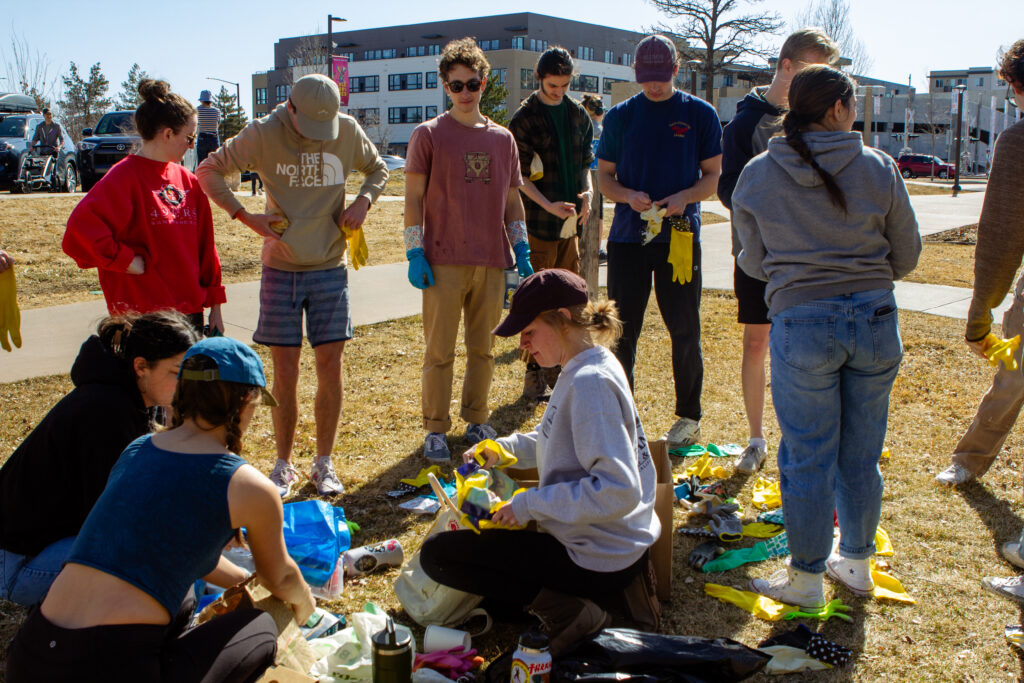 A large group of people stand around a pile of rubber gloves outside.