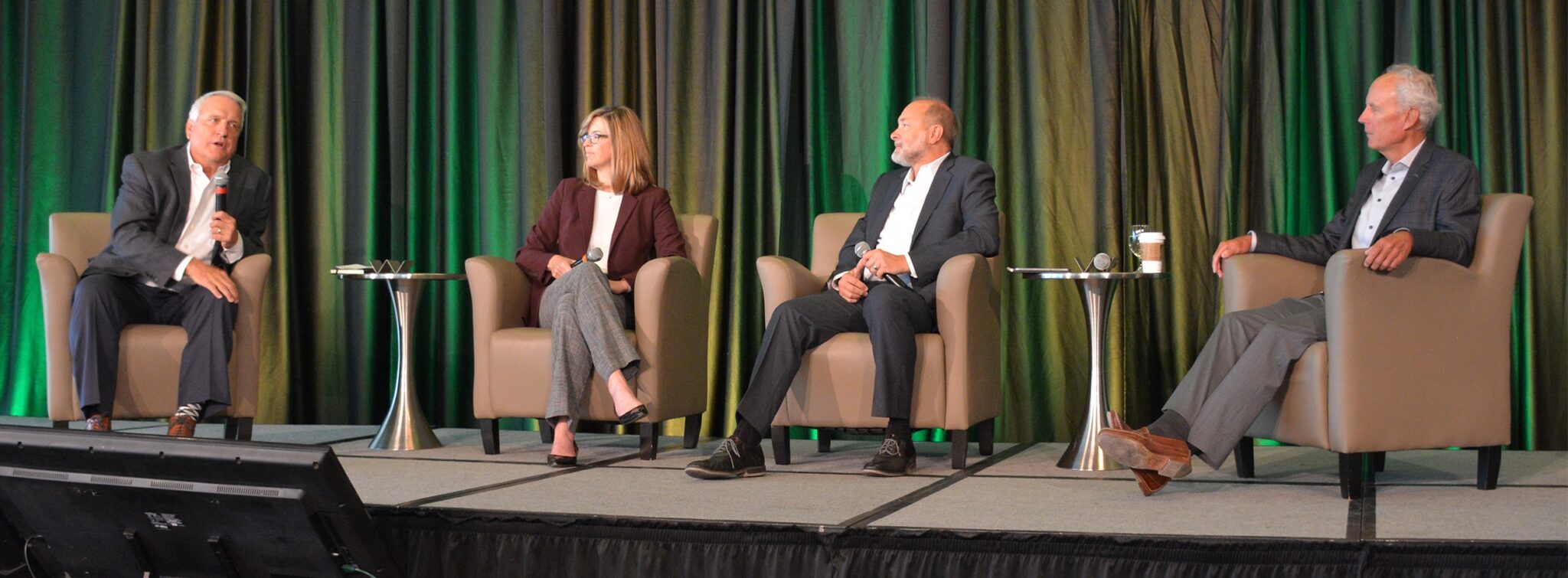 Four people sitting in chairs on a stage talking.