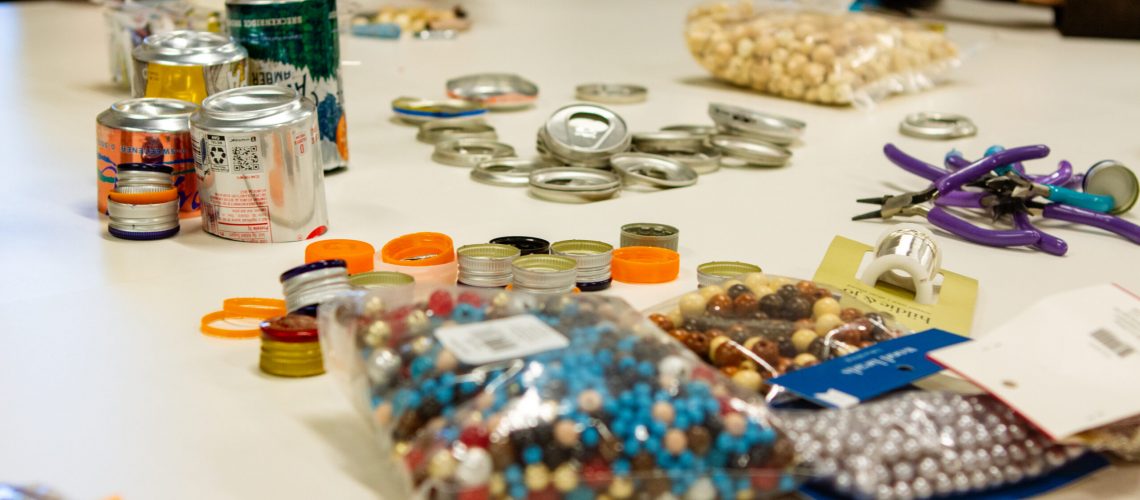 Old cans, beads, and other recycled trash sits upon a table inside.