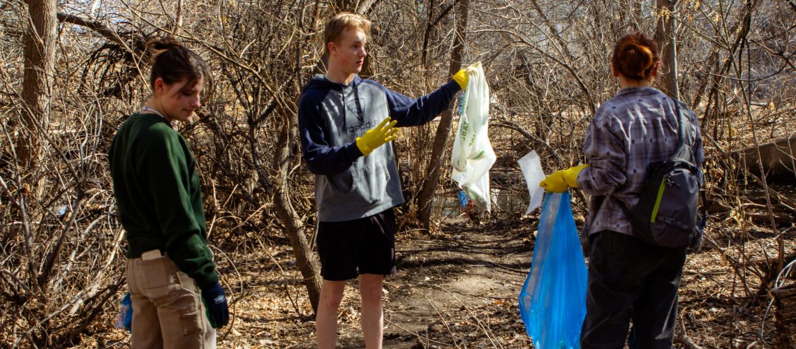 Three people carry trash bags and clean trash in a park.